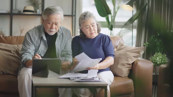 old retired asian senior couple checking and calculate financial billing together on sofa