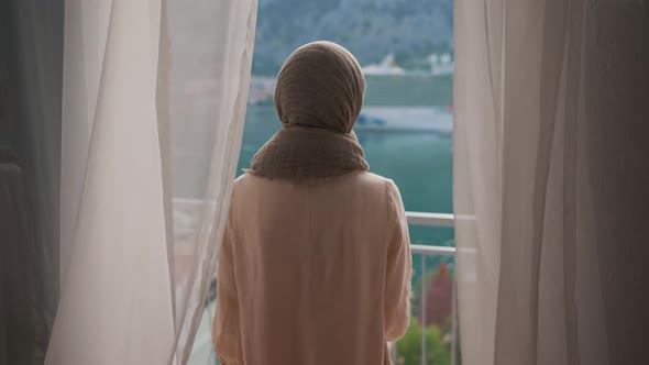 Arab Young Muslim Woman in Hijab Opening Curtain Lace Enjoying Drinking Hot Coffee or Tea Watching alt