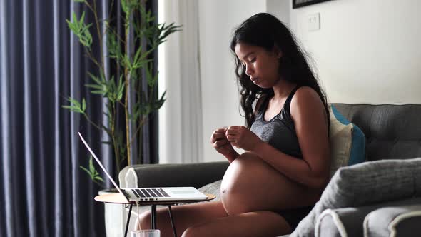 Pregnant Woman Working at Home Drinks Her Vitamins and Touching Her Big Tummy alt