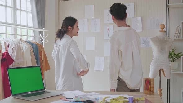 Two Asian Fashion Designers Choosing And Pinning To The Wall Clothing Sketches, Green Screen Laptop alt