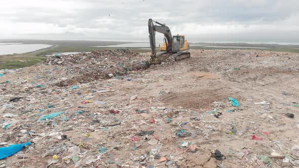 Digger clearing rubbish piled on a landfill full of trash alt