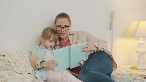Happy Young Family Mother and Daughter Are Reading Children's Book in Bed at Home alt