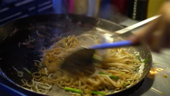 Thai street food vendor cooking and stirring delicious spicy Pad Thai dish in hot pan