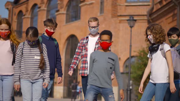 Portrait of Mixed-races Pupils Standing with Male Teacher at Schoolyard in Masks Holding Usa Flag alt