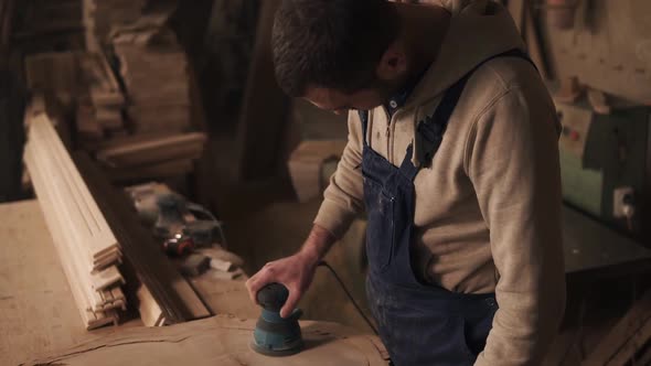 The Joiner Finishes Grinding the Piece of Wood Turns Off the Grinder and Checks the Surface for alt