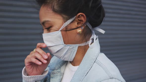 Mixed race woman coughing on her medical coronavirus mask alt