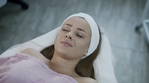 Pretty Young Woman Lies on Couch in Cosmetology Clinic Opens Eyes and Looks Up alt