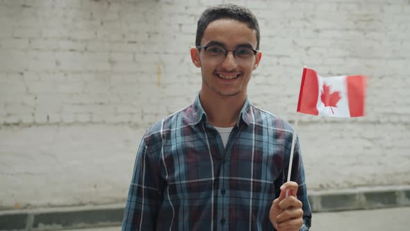Slow Motion of Middle Eastern Man Waving Canadian Flag and Smiling Standing Against Brick Wall alt