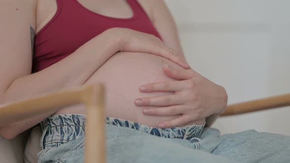 Close Up of Pregnant Woman Stokes Her Big Belly While Sitting on Chair alt