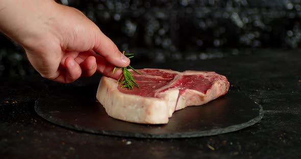 The Men's Hand Puts Rosemary on a Steak Raw Beef T-bone alt