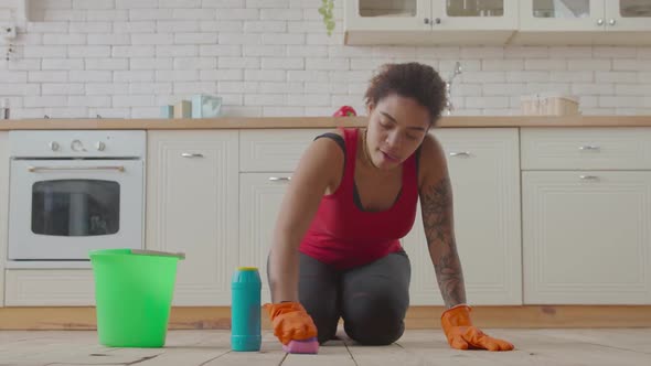 Kneeling African Woman Wiping Floor with Detergent alt