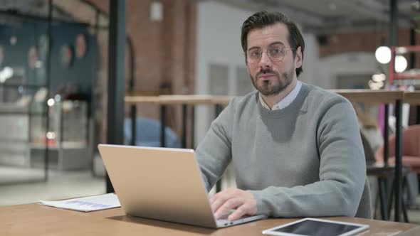 Young Man Looking at Camera While Using Laptop in Office alt