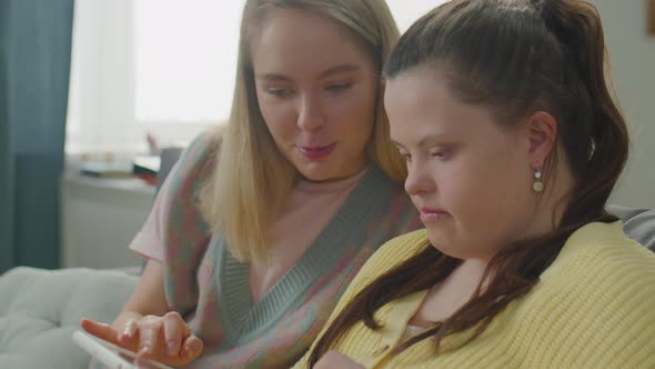 Woman and Girl with Down Syndrome Using Tablet and Talking alt
