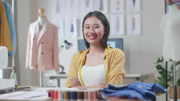 Female Designer With Measuring Tape Around Her Neck Smiling And Crossing Her Arms To The Camera alt