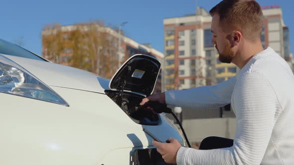 A Fairskinned Male Driver Connects an Electric Car to the Power System to Charge the Car Battery and alt