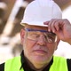 Close Up Portrait of Mature Master Builder in White Safety Hard Hat Looking at Camera Standing at - VideoHive Item for Sale