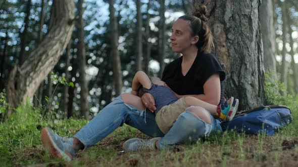 Calm woman breastfeeding her baby son while resting in the camp in forest at vacation alt