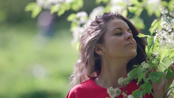 Relaxed Woman is Smelling Blooming Jasmine Tree in Spring Garden at Sunny Day alt