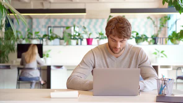 Young Casual Man Working on Laptop in Office  Female Colleague Brings Him Drink in a Cup alt