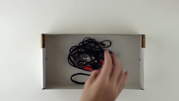 A Woman's Hand Folds Different Wires From Electra Devices Into a Cardboard Box