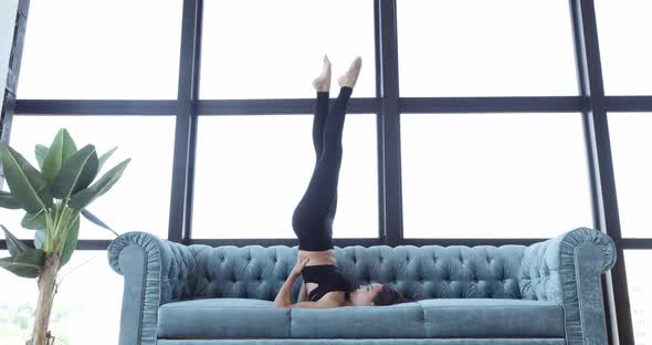 Sexy Girl Doing Exercises While Lying on Blue Sofa. Active Athletic Woman Exercising at Home Lazy alt