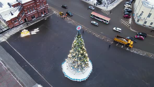 Luxurious Christmas Tree with Glowing Garlands in the City Square Aerial View alt