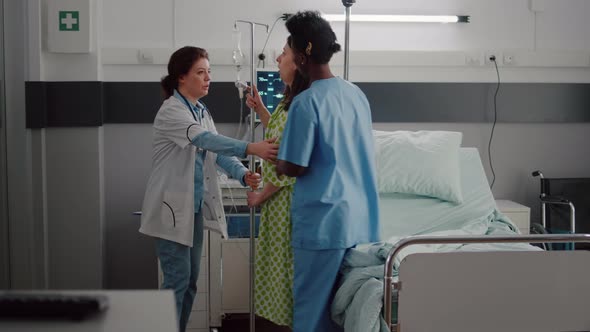 Medical Team Helping Patient to Stand Up From Bed Holding Intravenous IV Fluid Drip Bag alt