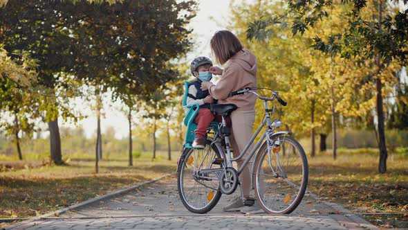 Mom Puts on a Medical Mask To Little Son Before Cycling alt