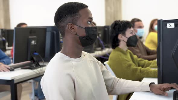 Young multiracial students using computer while wearing safety face mask for coronavirus outbreak
