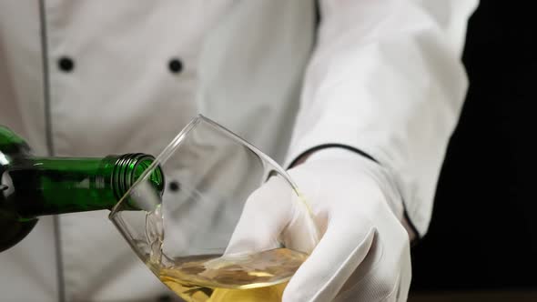 White wine pouring from bottle into glass on black background. HD alt