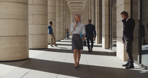 Beautiful Young Woman Walking and Talking on Mobile Phone Outside Business Center alt