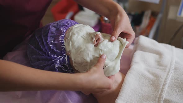 Beautician Removes the Hardened Mask From the Face of the Patient in the Spa Salon
