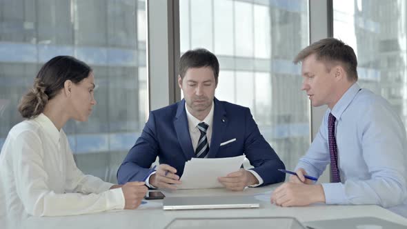 Middle Aged Businessman Having Reading Documents with His Assistants in Boardroom alt