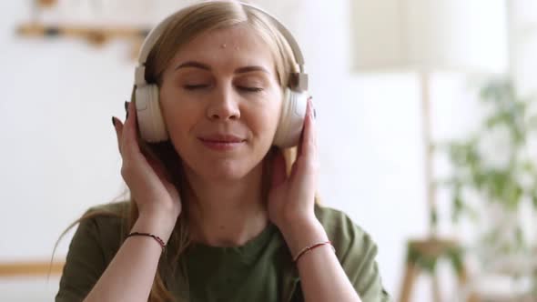 Cute Blonde Closeup Listening to Music with White Headphones in the Room and Dancing alt