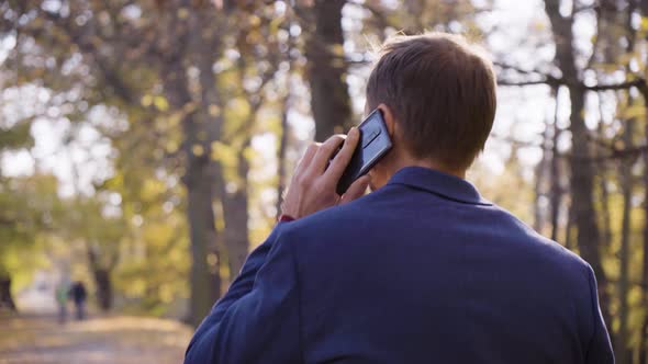 A Middleaged Handsome Caucasian Man Talks on a Smartphone As He Walks in a Park in Fall