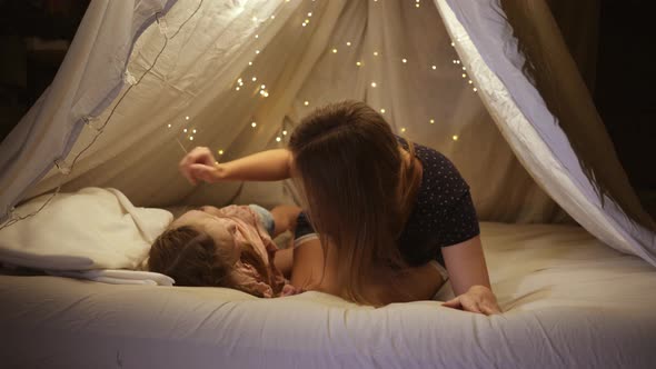 Happy Mom and Daughter Play with Each Other in a Homemade Tent at Home They Laugh and Hug