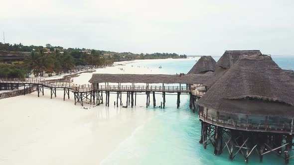 Flying Over African Wooden House With Pier On Stilts With Thatched Roof.