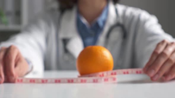 A Dietician Pulls An Orange With A Measuring Tape. An Orange Lies On The Table With A Measuring alt