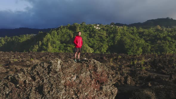 A Man Wearing Red Jacket Standing on a Mountain Peak in Rays of Evening Sun