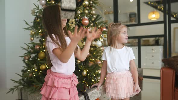 Charming Little Girls Holds a Gifts on a Background of Christmas Trees alt
