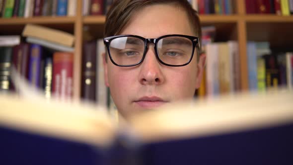 A Young Man Is Reading a Book in a Library. A Man with Glasses Carefully Looks at the Book Closeup alt
