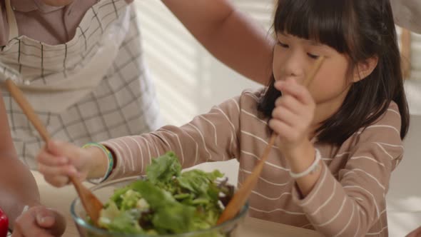 Family Mother, Father, and Cute Little Girl cooking salad spending time together in the kitchen.