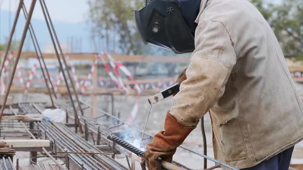 Welder at Construction Site Is Welding Pipe with Electrode in Helmet. alt