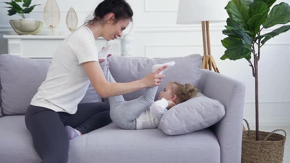 Young Mother Playing with Her Cute one year Daughter on the Couch at Home alt