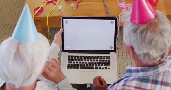 Rear view of senior caucasian couple celebrating birthday while having a video call on laptop at hom alt
