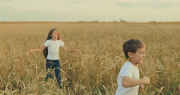Beautiful Girl with Long Hair and a Boy are Running Along a Wheat Field