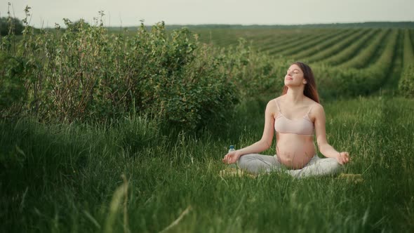 Pregnant woman with dark hair in a pink top and light pants enjoys the sun outdoors.