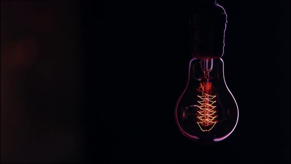 Decorative vintage light bulb hangs and shines in the dark copy space