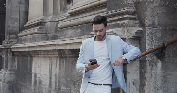 Young Man Near The Ancient Castle In A Festive Light Suit Talking On The Phone alt