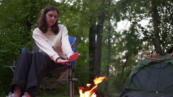 Lonely Woman Sits By the Fire Next to a Tent in the Woods
